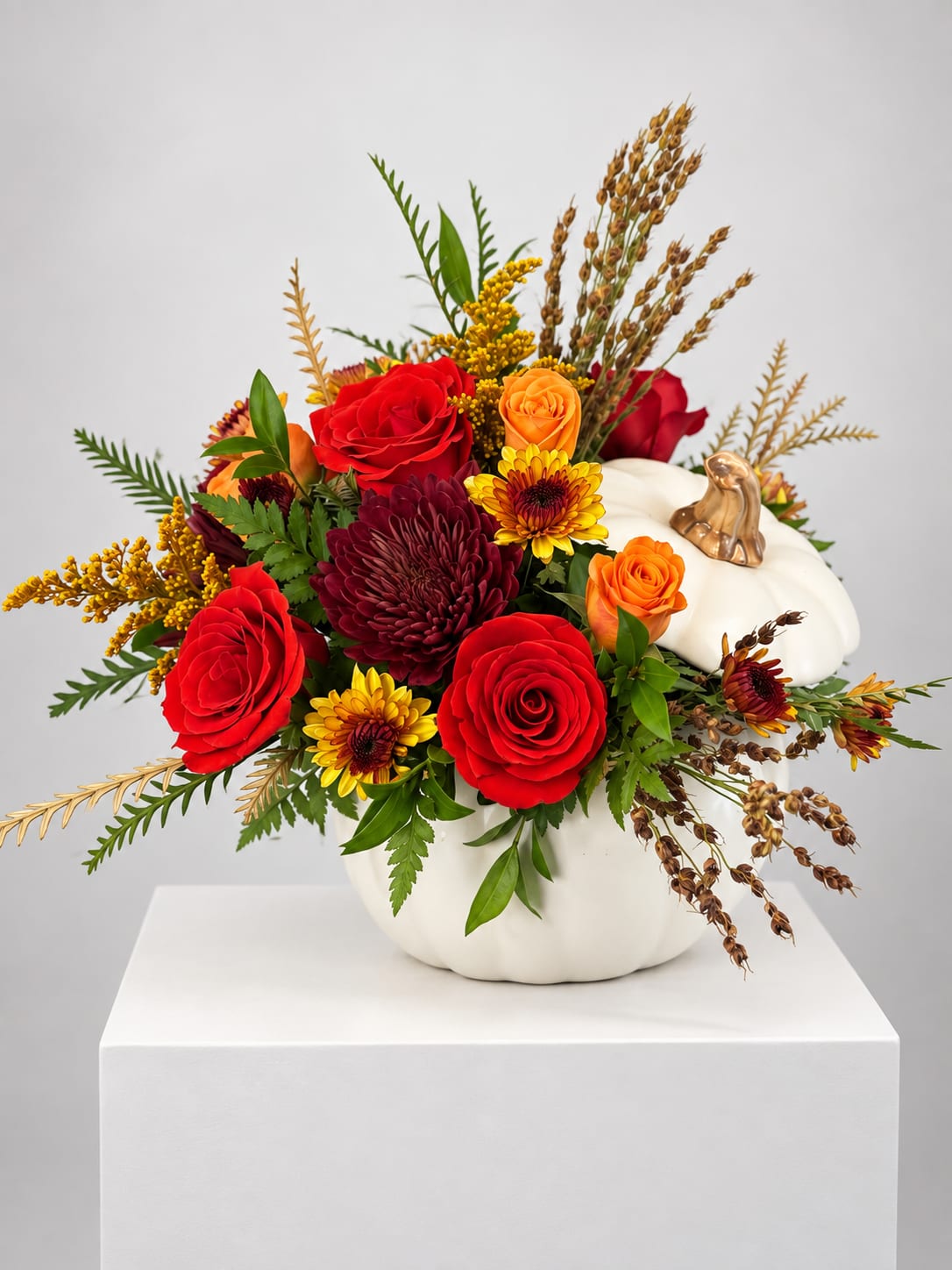 Autumn floral arrangement in a white pumpkin container with red and orange blooms
