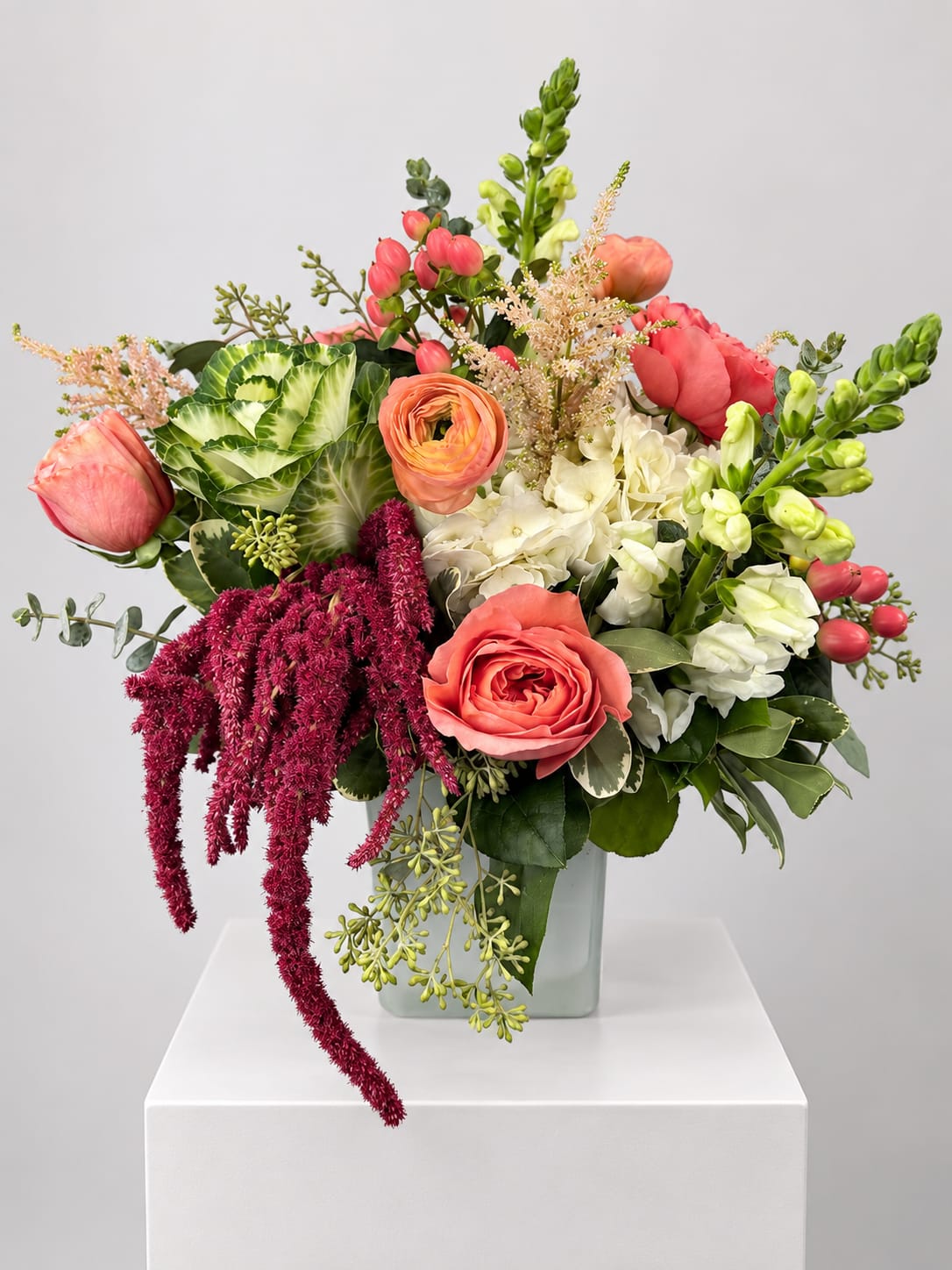 Mixed bouquet with coral roses, white blooms, and green snapdragons in a glass vase
