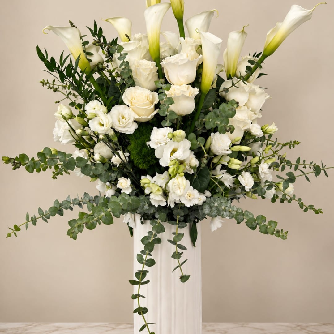 White calla lilies and roses in a tall white vase with trailing greenery
