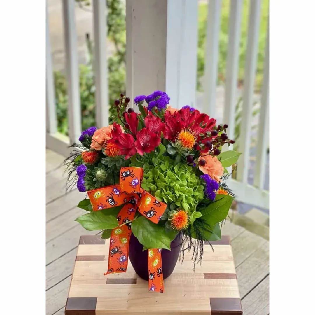 Colorful floral arrangement in a purple vase with an orange ribbon