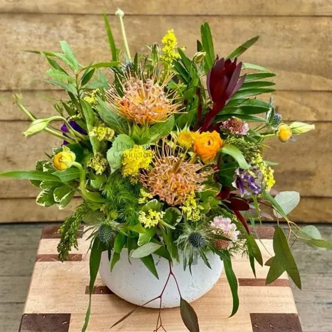 Mixed floral arrangement in a white bowl vase with yellow, burgundy, and purple blooms