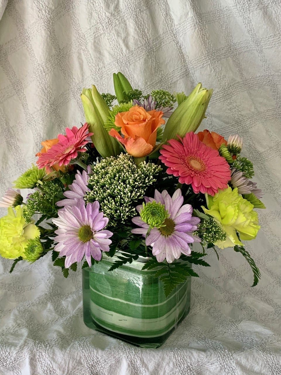 Mixed bouquet in a green glass vase with pink, orange, and lavender flowers