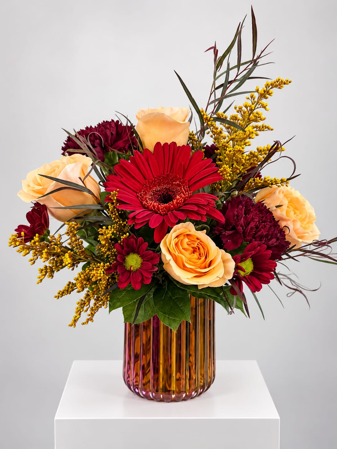Mixed bouquet of red and peach flowers in an amber glass vase