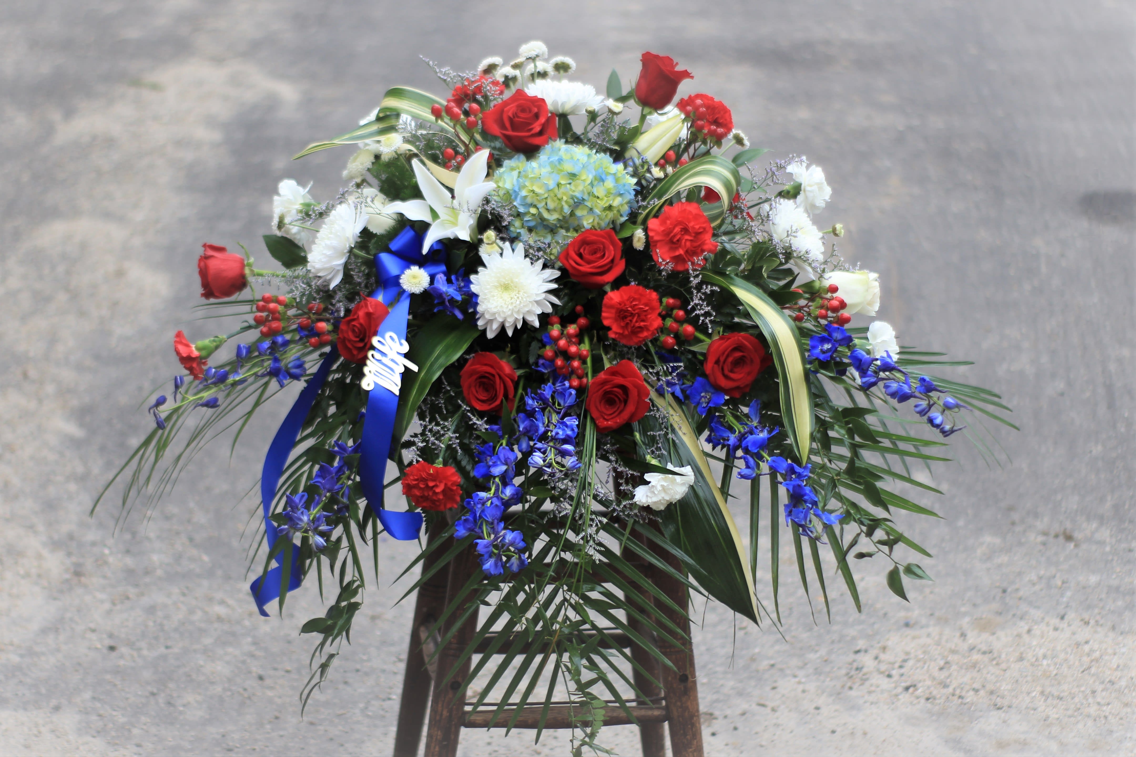 Large floral arrangement with red roses, white lilies, and blue flowers on a stand