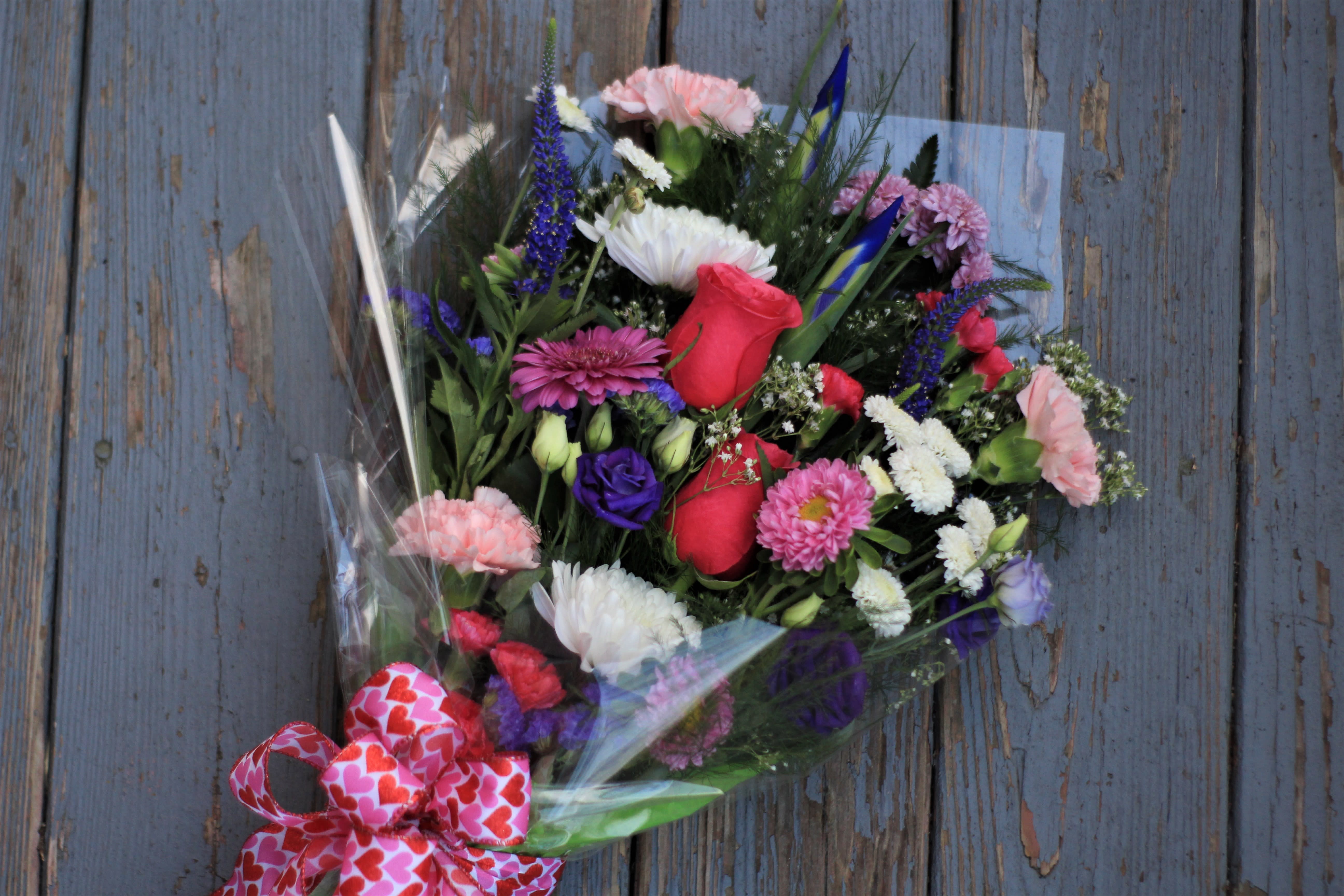 Mixed bouquet of roses, carnations, and daisies wrapped in clear plastic