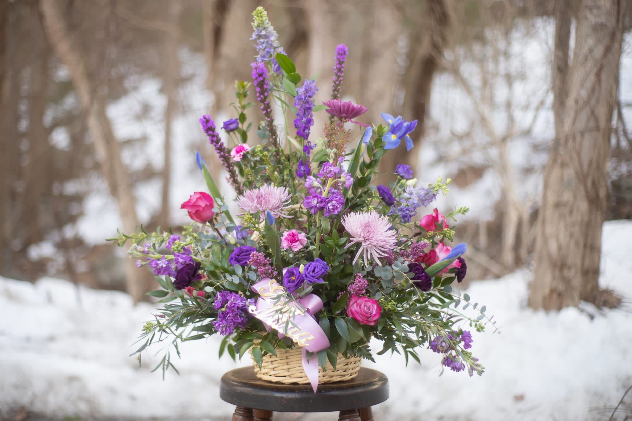 Basket arrangement of purple and pink flowers with a lavender ribbon