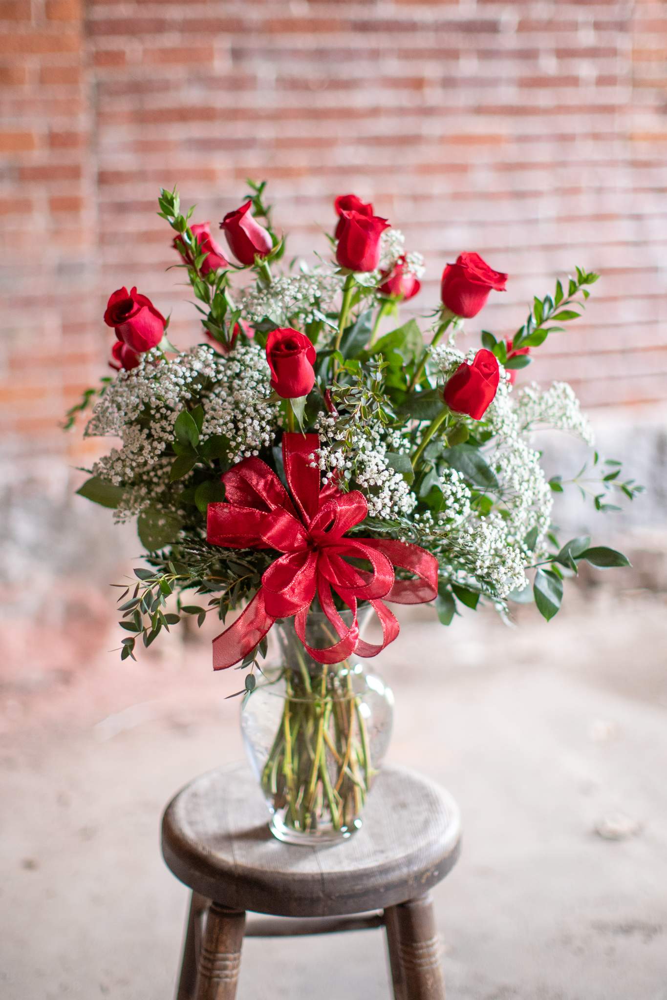 Red roses and baby's breath in a clear glass vase with a red ribbon