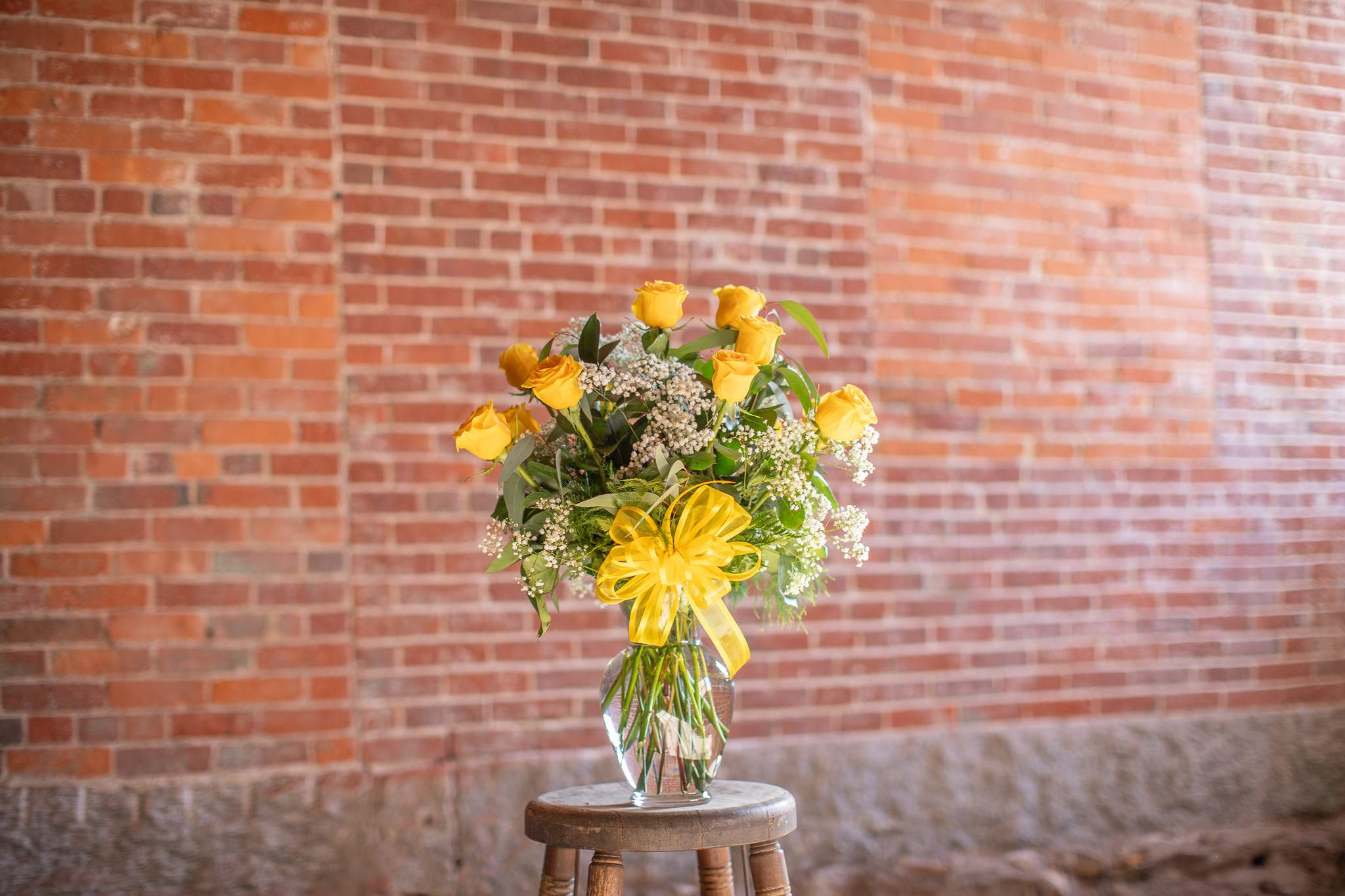 Yellow rose bouquet in a clear glass vase with a yellow ribbon