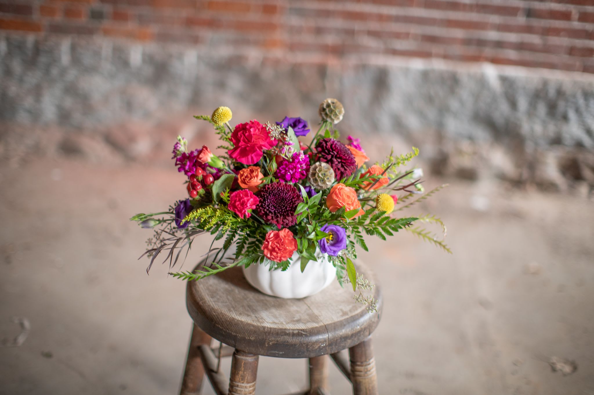 Colorful mixed bouquet in a white pumpkin-shaped vase on a wooden stool