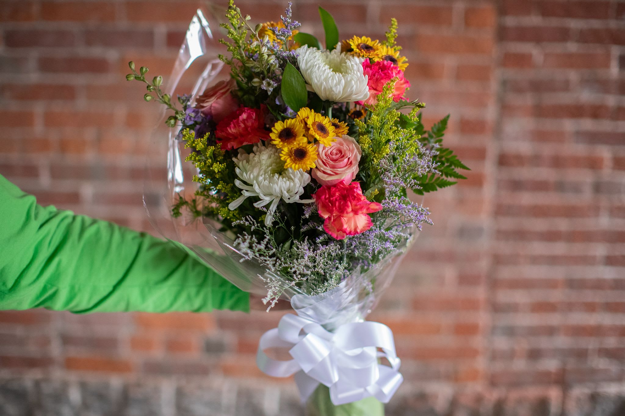 Mixed bouquet of colorful flowers wrapped in clear plastic with a white ribbon