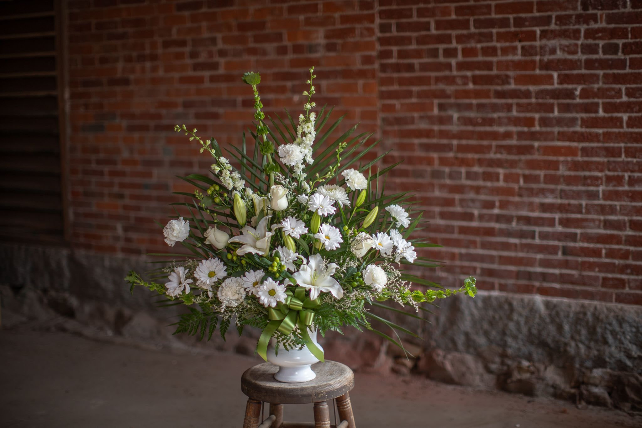 White floral arrangement in a white vase with a green ribbon