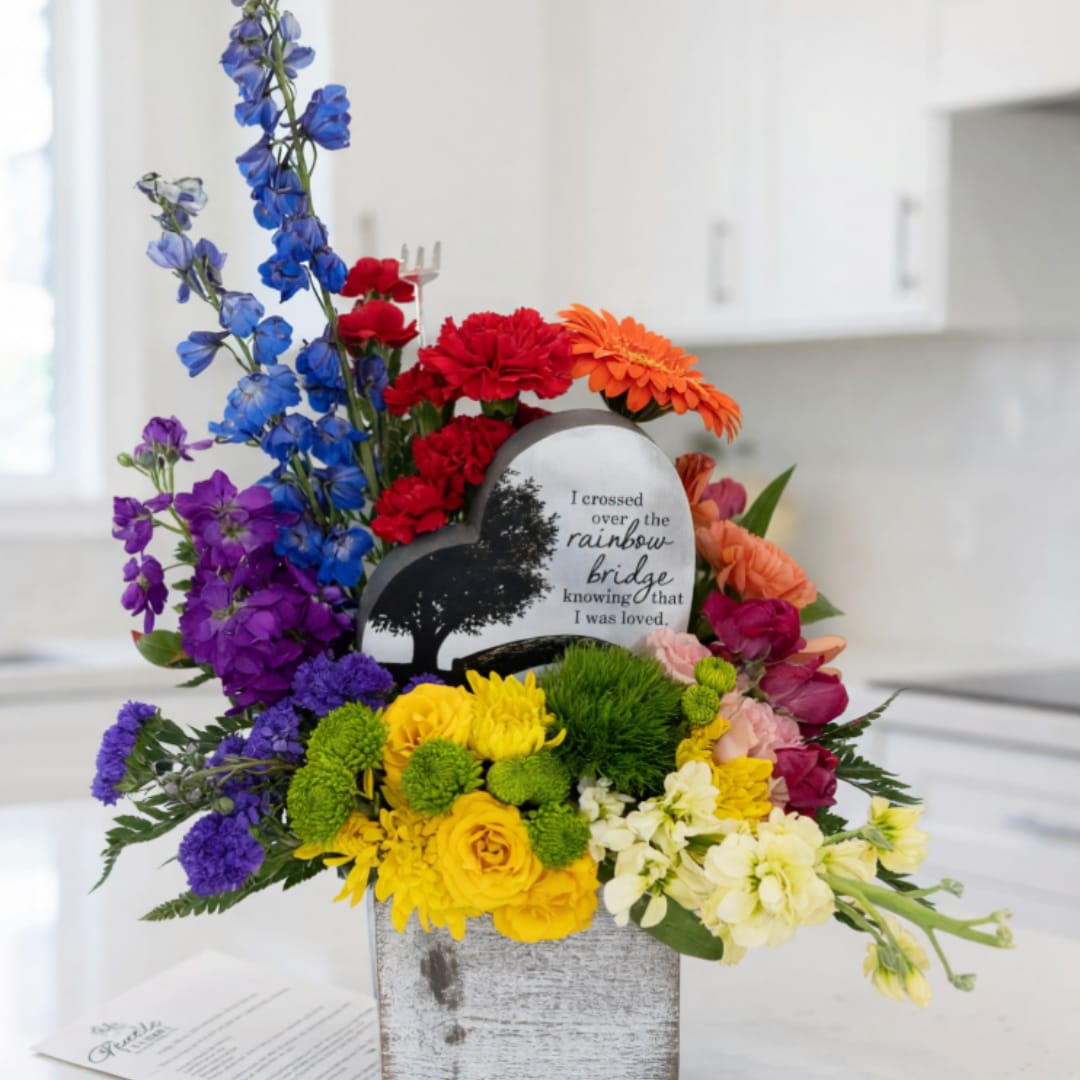 Rainbow-colored floral arrangement with a heart memorial plaque in a gray container