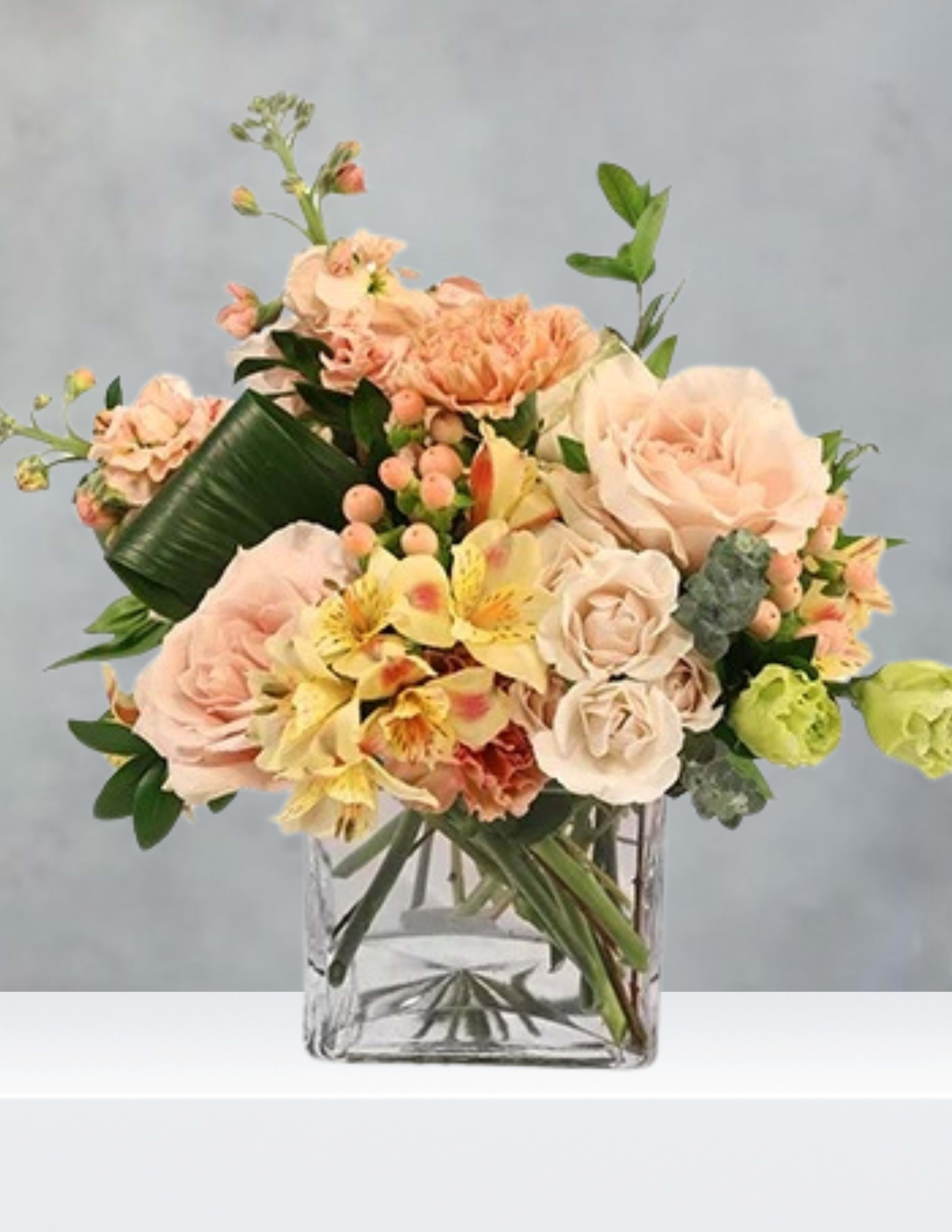Peach and cream bouquet in a clear square vase
