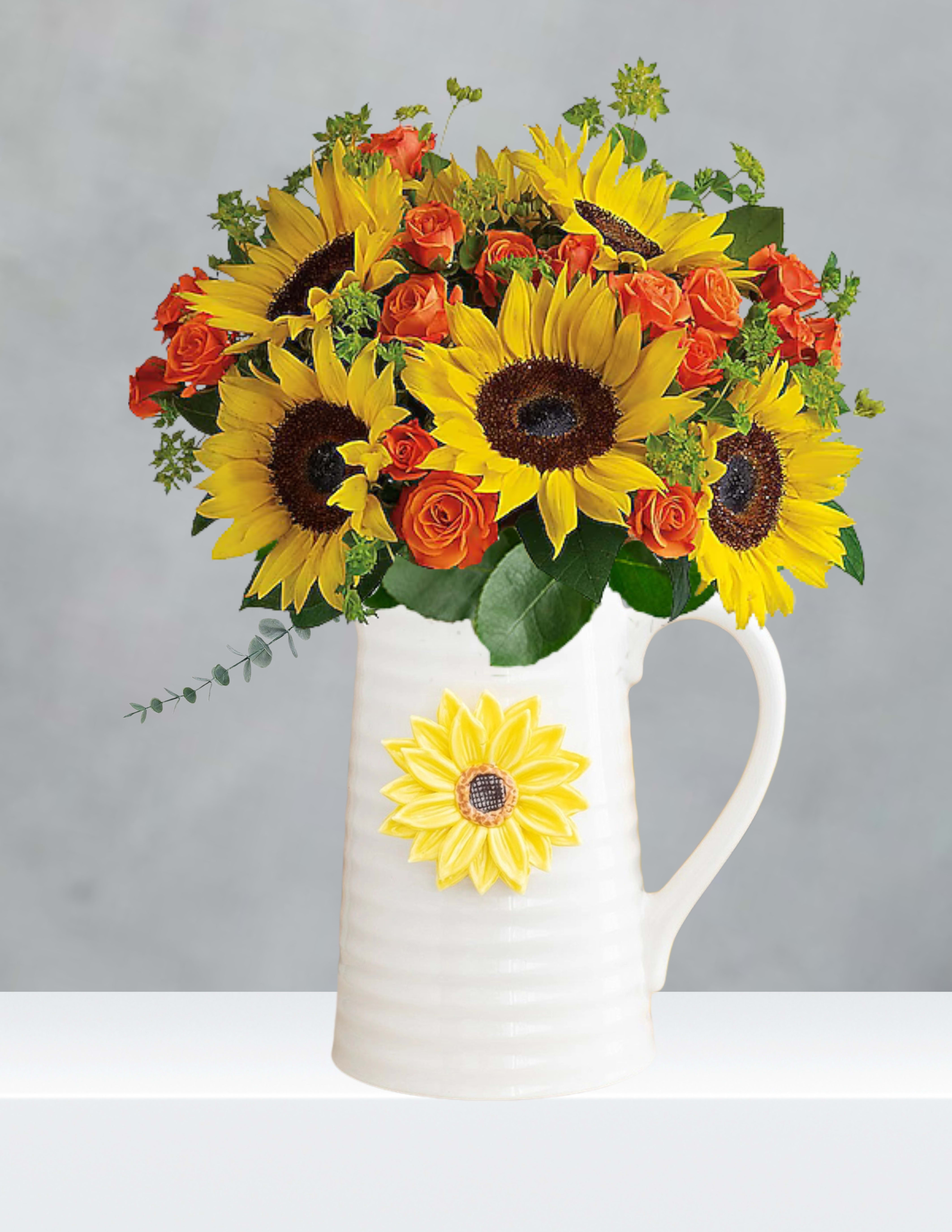 Sunflowers and orange roses arranged in a white pitcher vase
