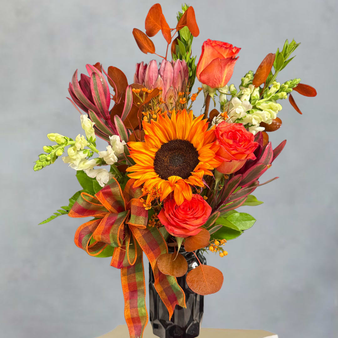 Orange sunflower and roses in a black vase with a plaid ribbon