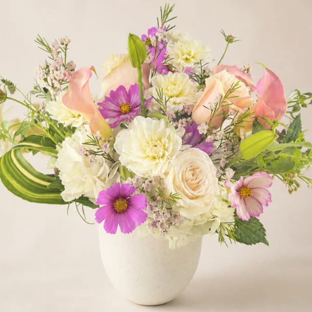 Mixed bouquet of pink, white, and purple flowers in a white vase