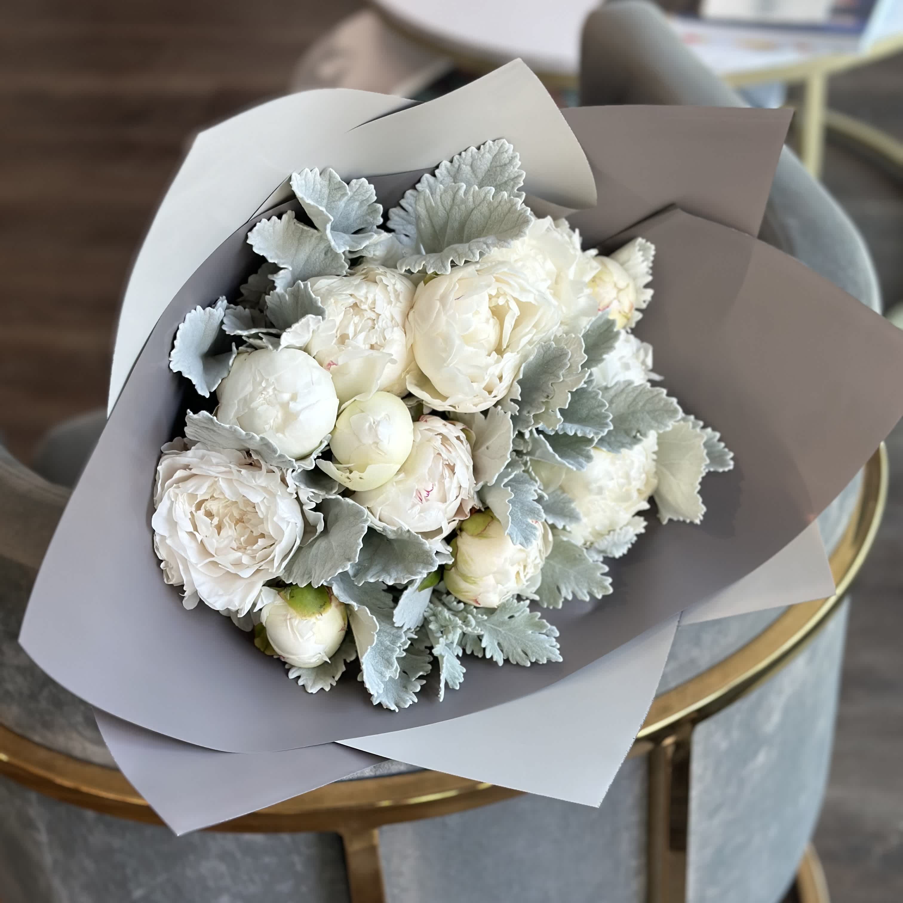 Bouquet of white peonies with silvery foliage in gray paper