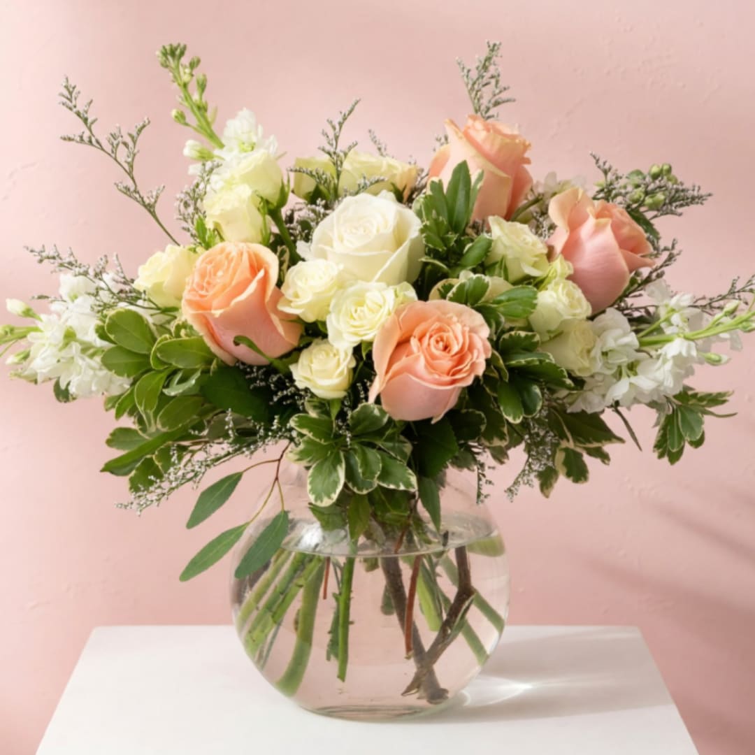 Peach and white roses arranged in a clear glass vase