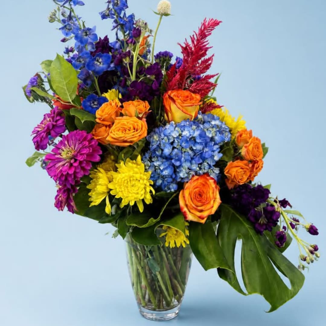 Colorful mixed bouquet in a clear glass vase with roses, hydrangea, and mums