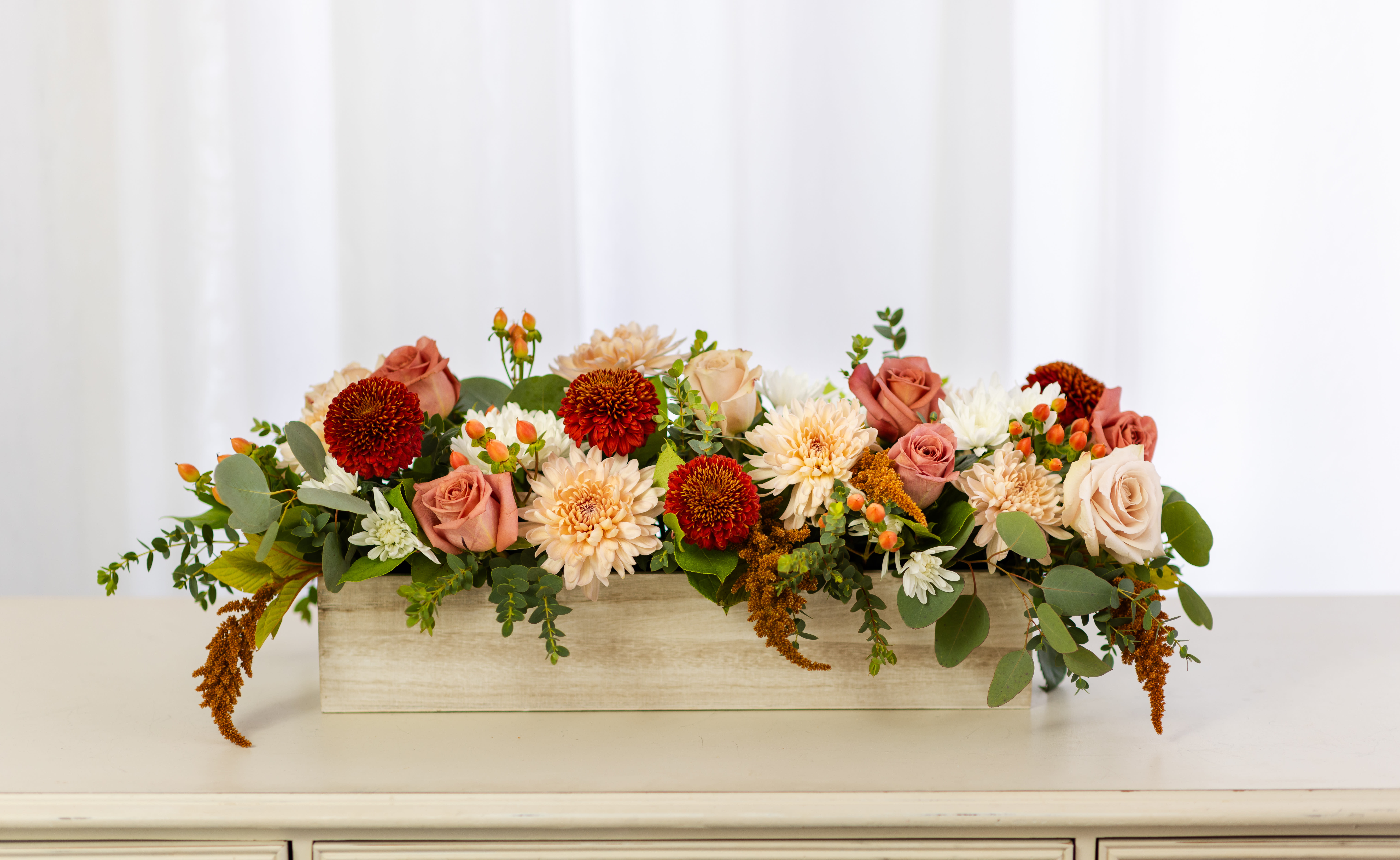 Chai Latte Collection - Large Wood Box  - All the cozy vibes of warm fall spices inspired our new Chai Latte Collection. Shades of cinnamon, mocha, and cream come together in a seasonal mix of mums, roses, berries, and branches—beautifully arranged in a white-washed wood box. An ideal gift for a friend or loved one, or the perfect centerpiece for a fall feast.  Product Details: This arrangement is approximately 24" long and 8" wide. The Deluxe size includes 10 additional stems of flowers and greenery. 