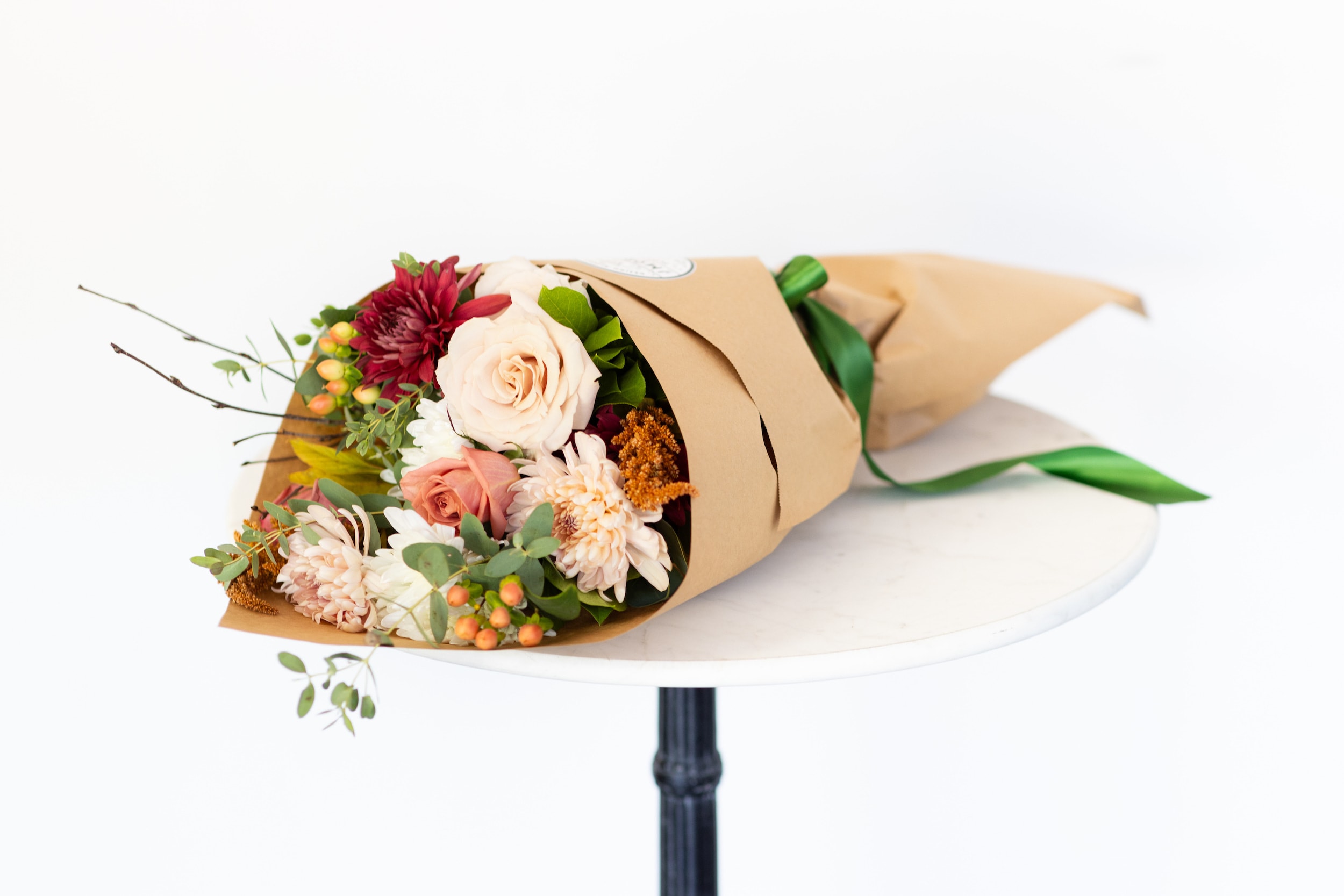 Chai Latte Collection - Wrapped Bouquet  - All the cozy vibes of warm fall spices inspired our new Chai Latte Collection. Shades of cinnamon, mocha, and cream come together in a seasonal gathering of mums, roses, berries, and branches—artfully arranged to capture the essence of autumn. Our wrapped bouquet makes a thoughtful gift for an anniversary, birthday, thank-you, get-well wish, or any special occasion.   Specifications: This arrangement is approximately 18" long by 12" wide. The DeLuxe and Premium Designs will have an additional 5 beautiful blooms. 