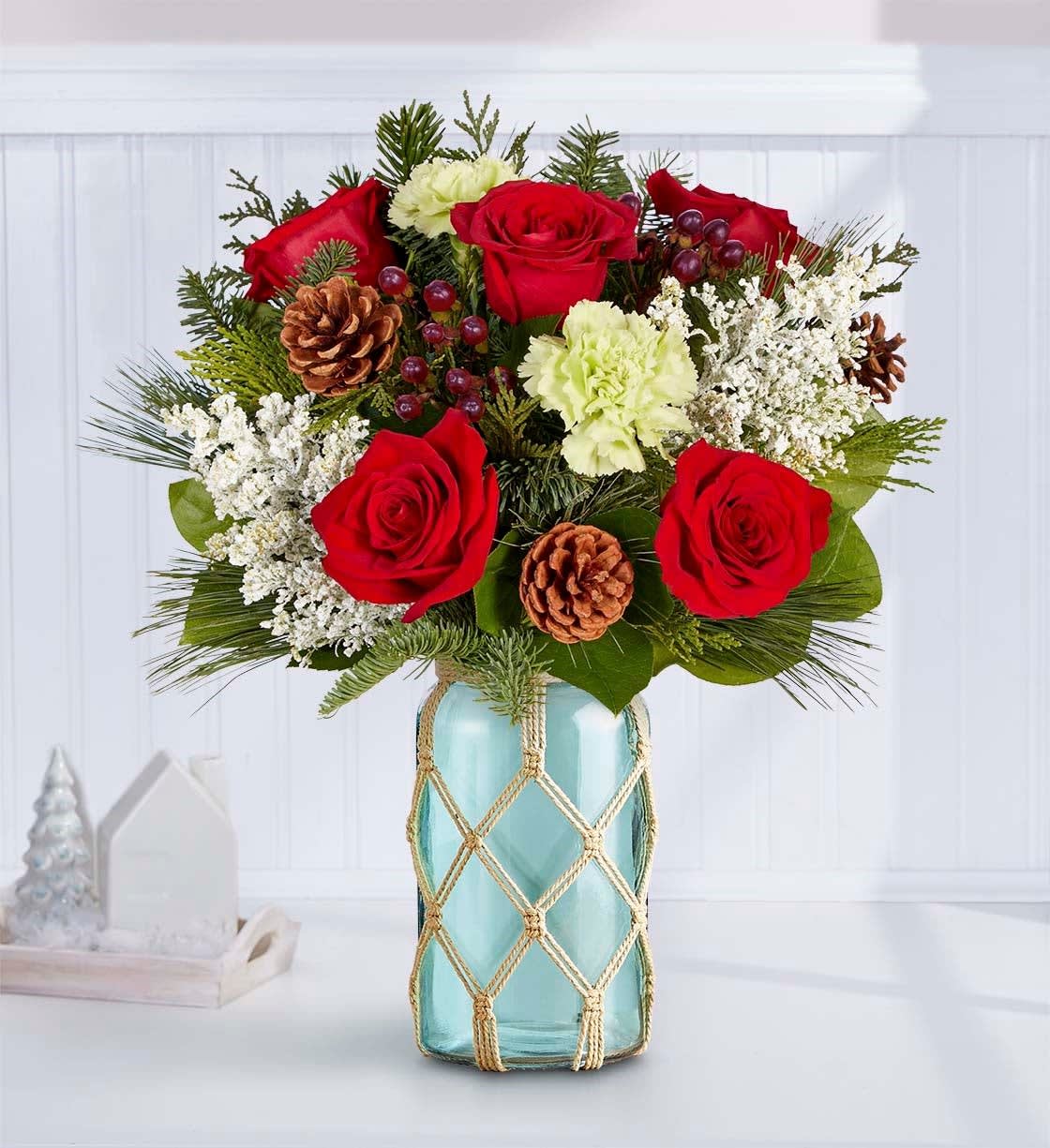 Red roses and white carnations in a blue glass vase with pinecones