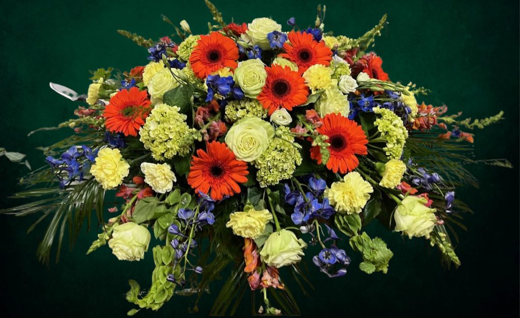 Large bouquet of orange gerbera daisies, pale roses, and blue flowers
