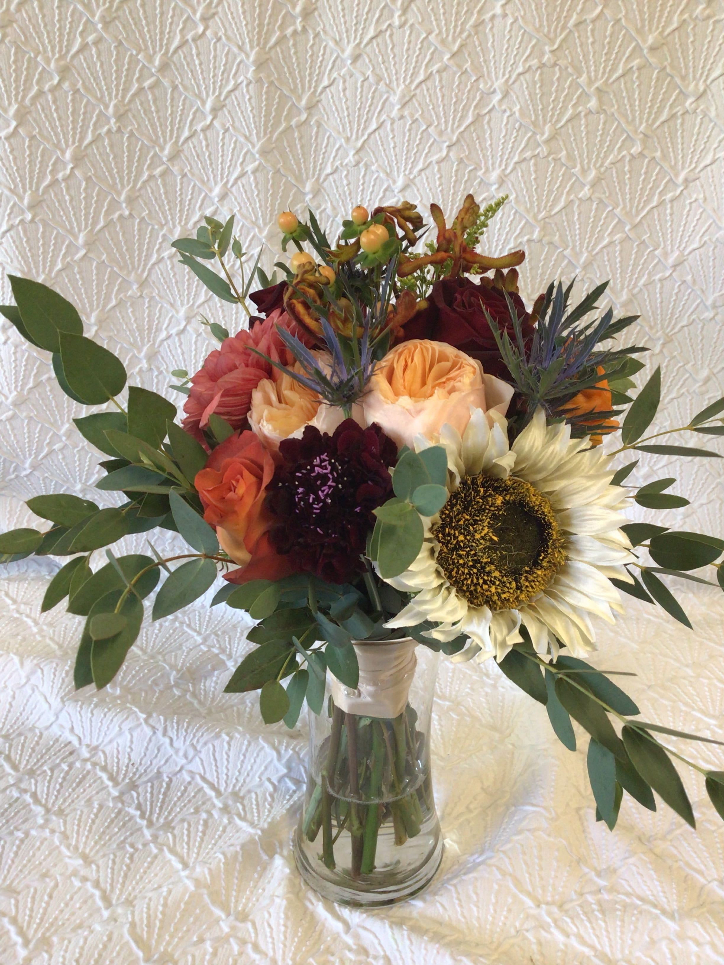Mixed bouquet with a sunflower, roses, and dark blooms in a glass vase