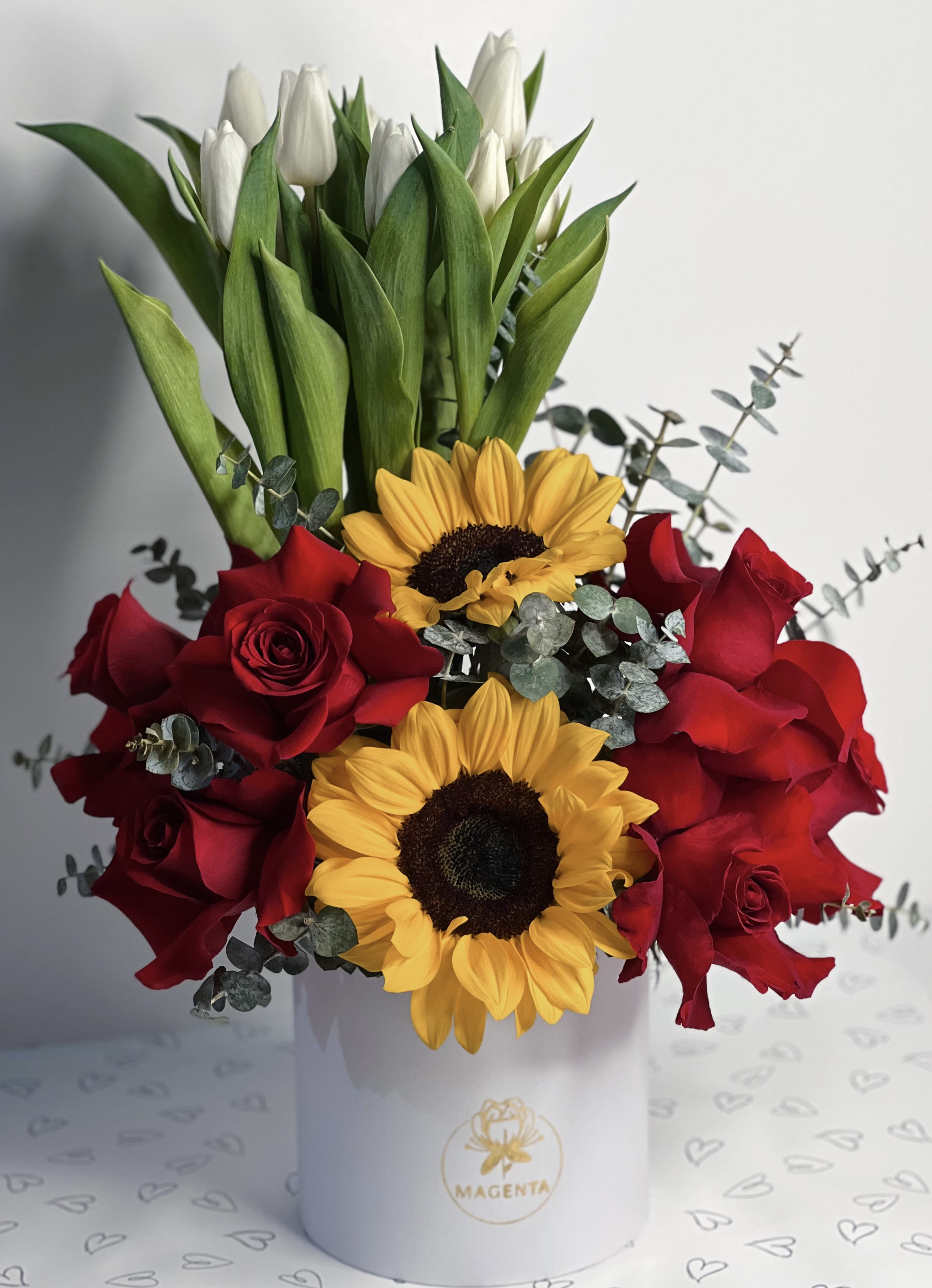 Red roses and sunflowers in a white hat box with white tulips