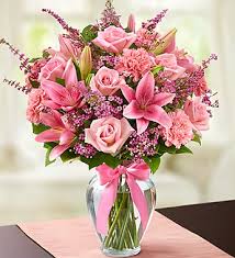 Pink bouquet of lilies, roses, and carnations in a glass vase with a ribbon
