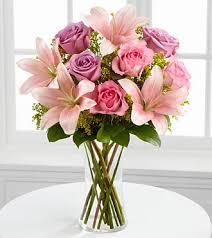 Pink and lavender roses with pale lilies in a clear glass vase