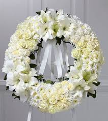 White floral funeral wreath with lilies and roses on a ribbon stand
