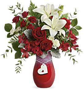 Red roses and white lilies in a red vase with a heart tag