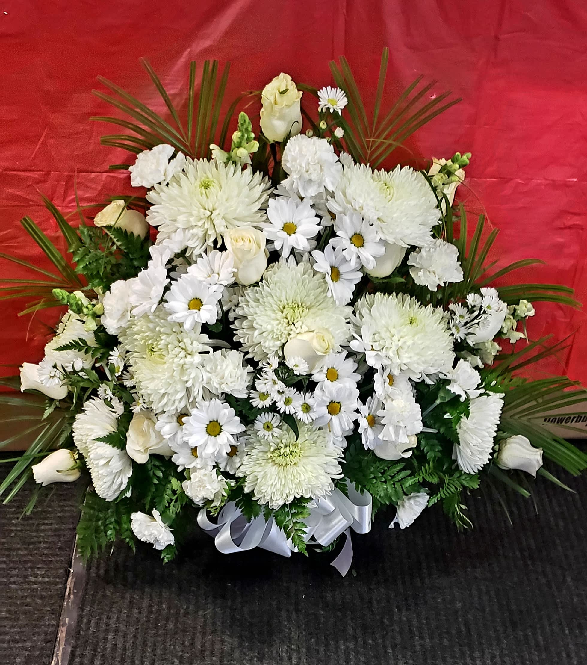 White floral arrangement with daisies and roses in a ribbon-tied base