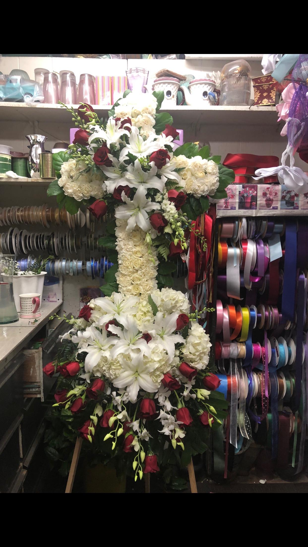 Tall floral cross with white lilies, cream roses, and red roses