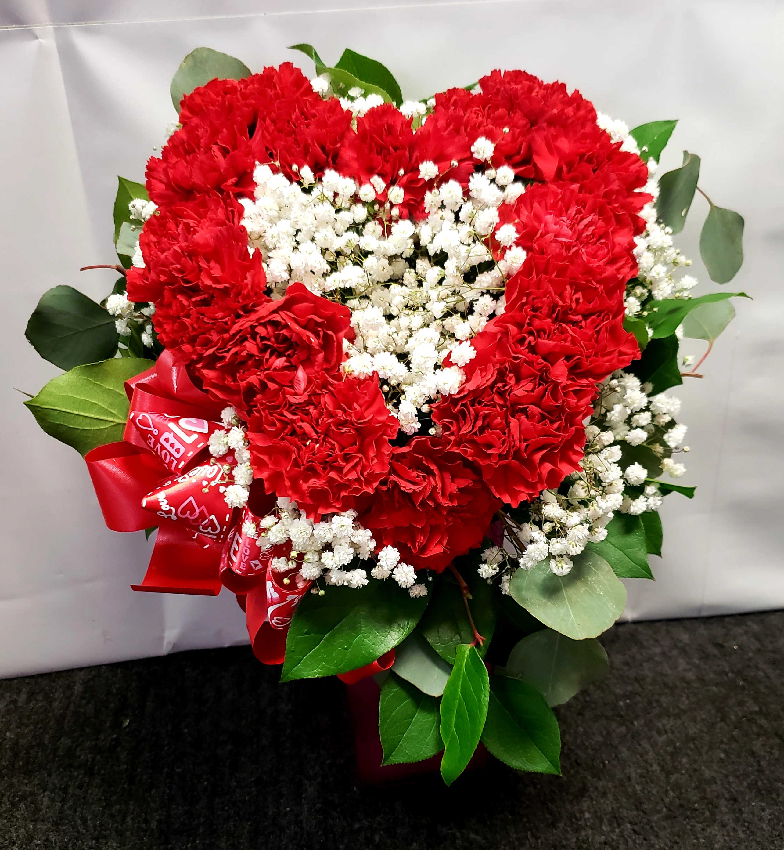Heart-shaped bouquet of red carnations with white baby's breath and a red ribbon
