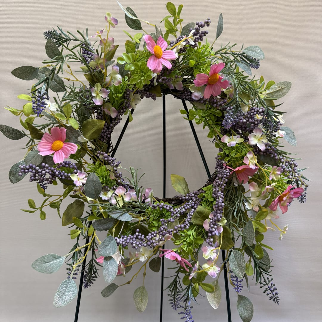 Floral wreath with pink daisy-like flowers and purple berries on a black stand
