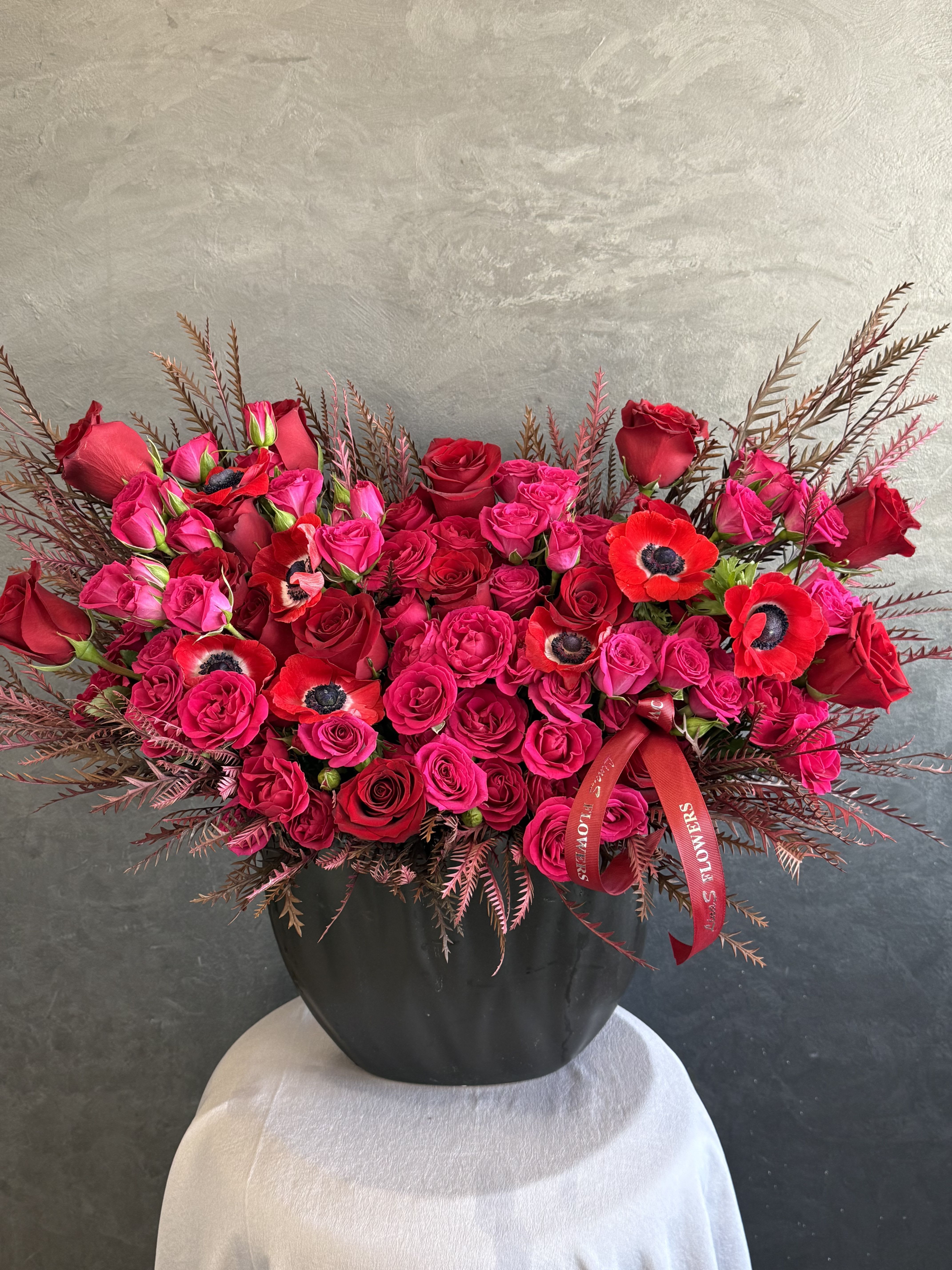 Red and hot pink roses arranged in a black vase with red ribbon