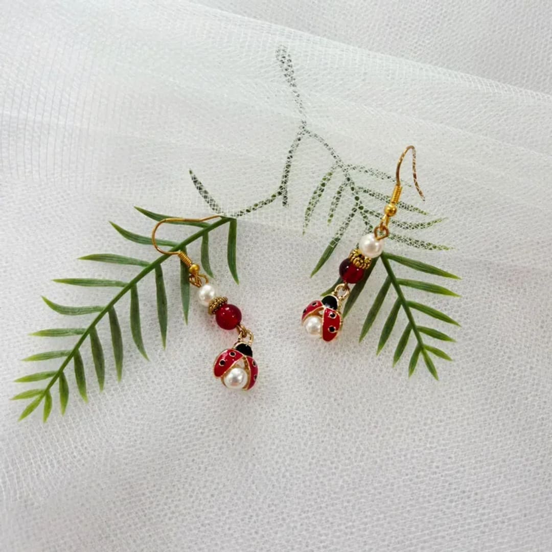 Pair of dangling ladybug earrings on a white textured fabric background