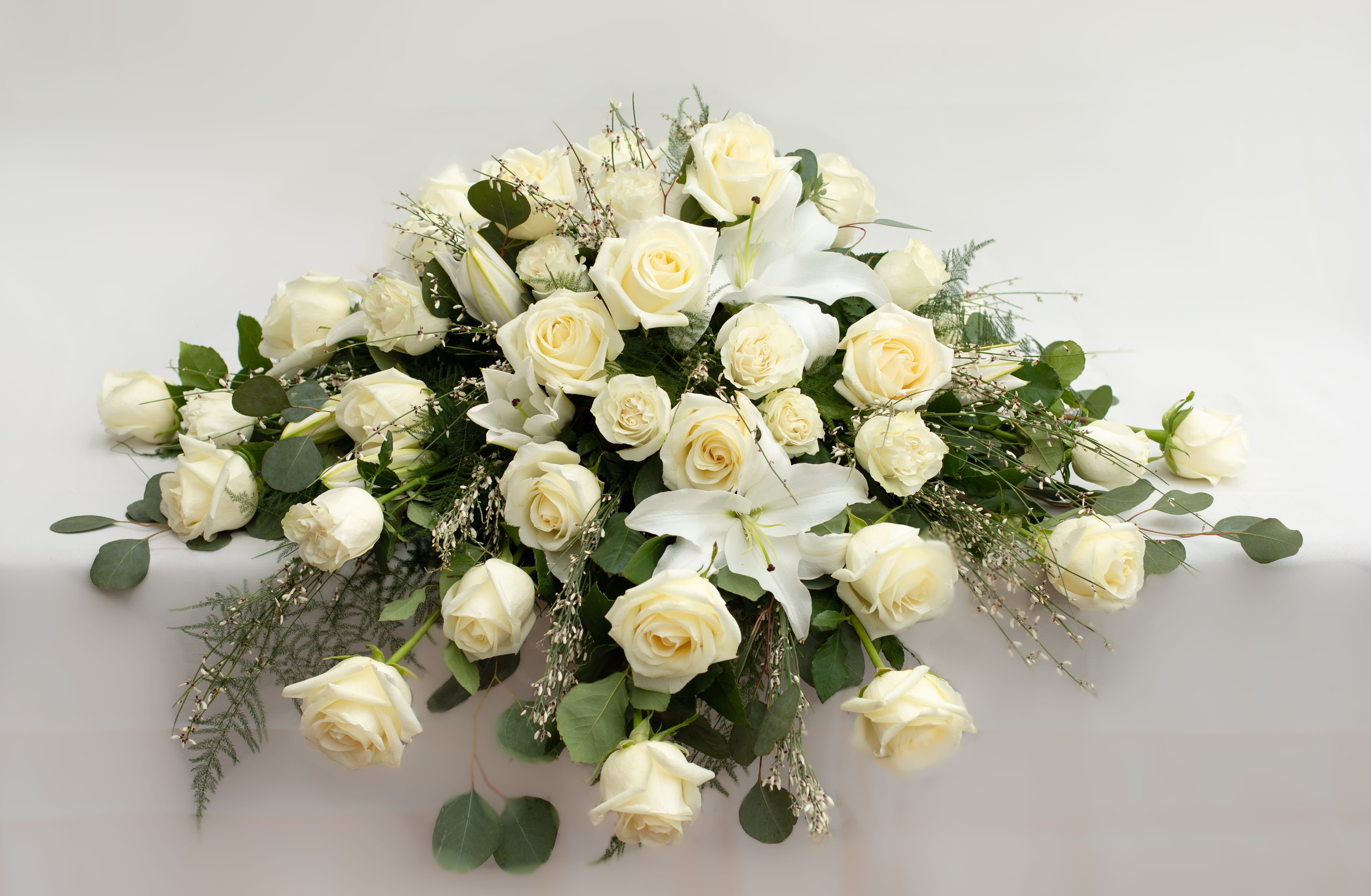 White rose and lily arrangement with greenery on a white surface