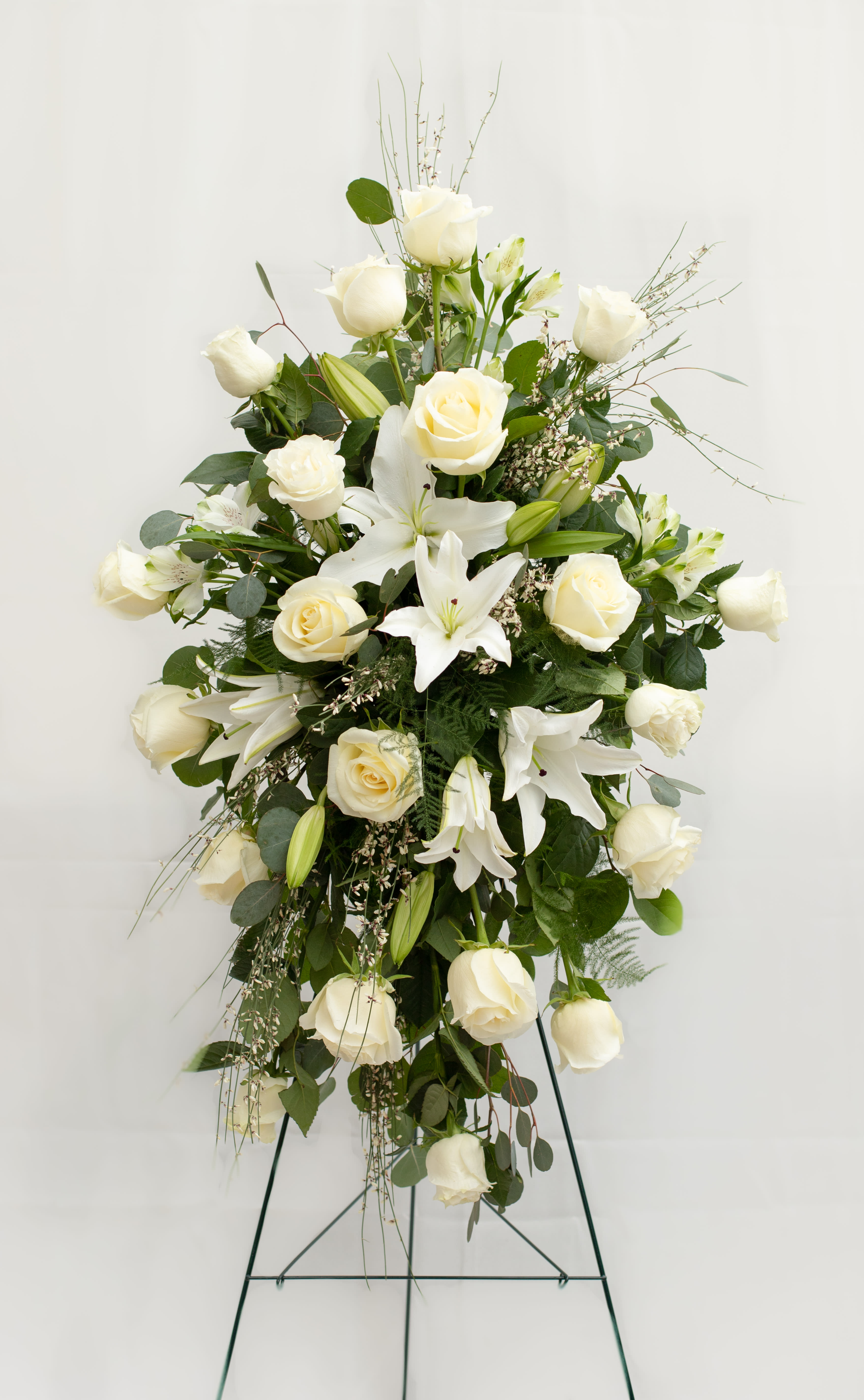Tall white floral standing spray with roses and lilies on a metal easel