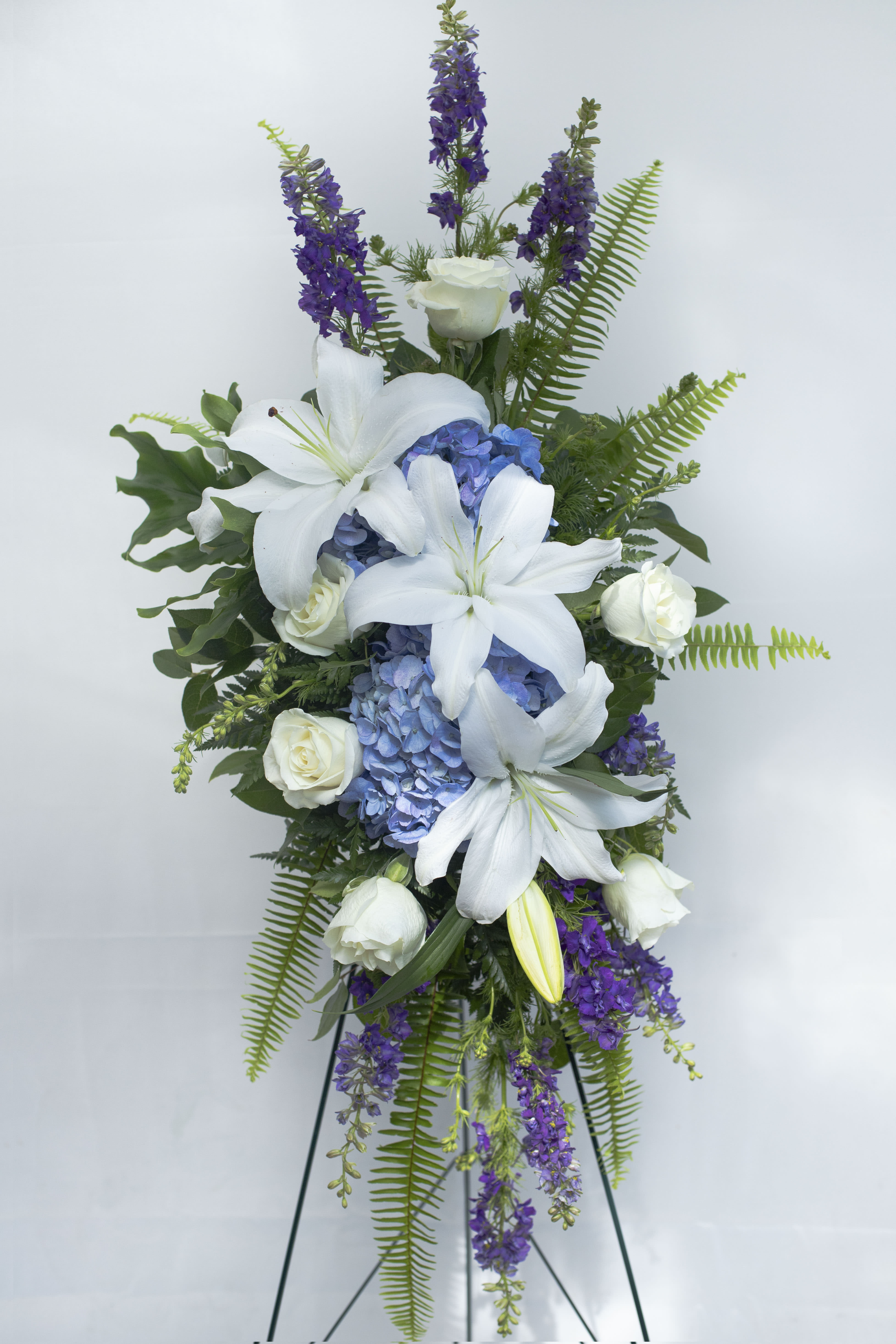 Tall floral spray with white lilies, blue hydrangeas, and purple flowers