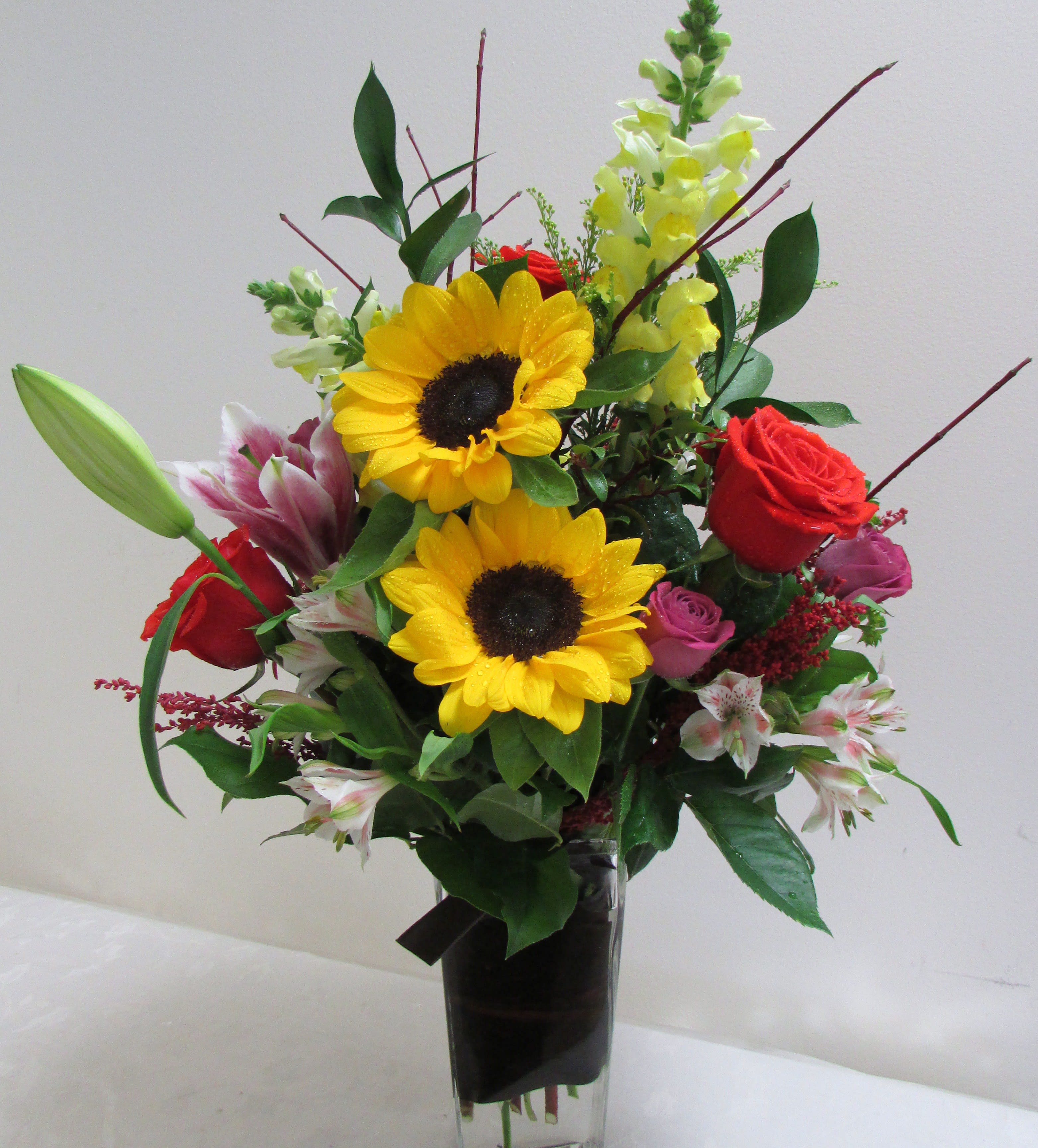 Mixed bouquet with sunflowers, roses, lilies, and snapdragons in a tall vase