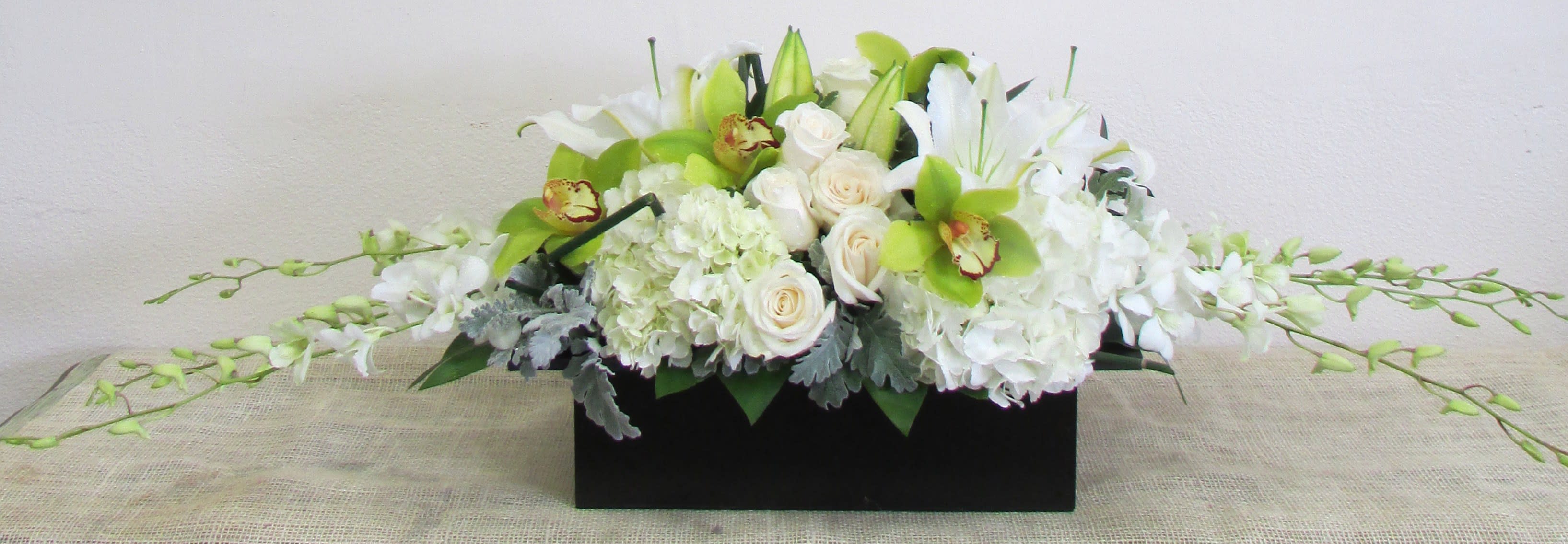 Chic piece - Simple, clean and classy is the best way to describe this stunning arrangement. An all white design with a touch of green cymbidium orchid in a wood pot. It's low profile makes it the perfect centerpiece.