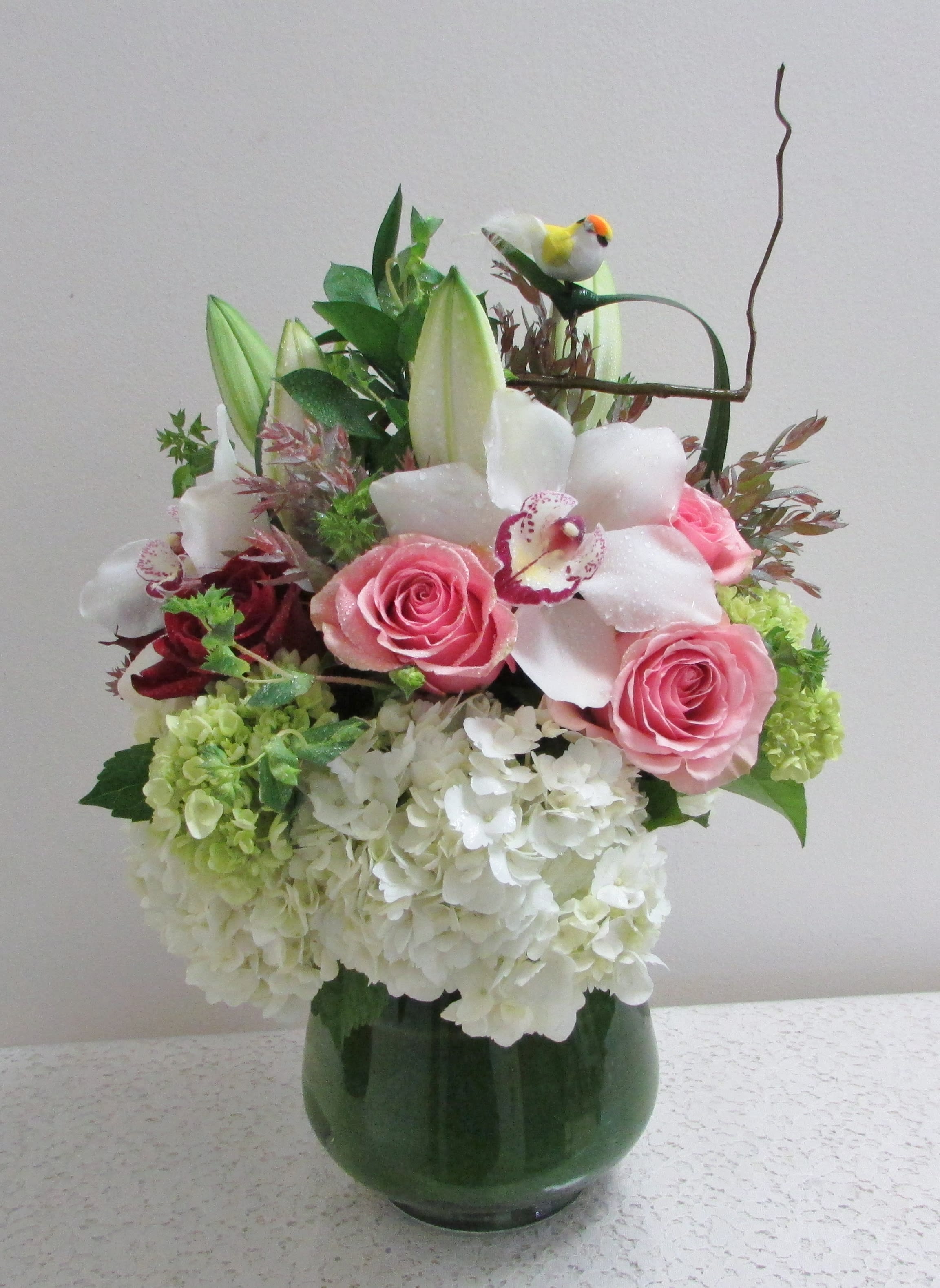 Birthday Surprise - A simple yet elegant arrangement to celebrate a special day. This arrangement is made up of hydrangea, roses, lilies, cymbidium orchid and a variety of other accents to give it a special touch in a shorter profile vase perfect to set bed side.