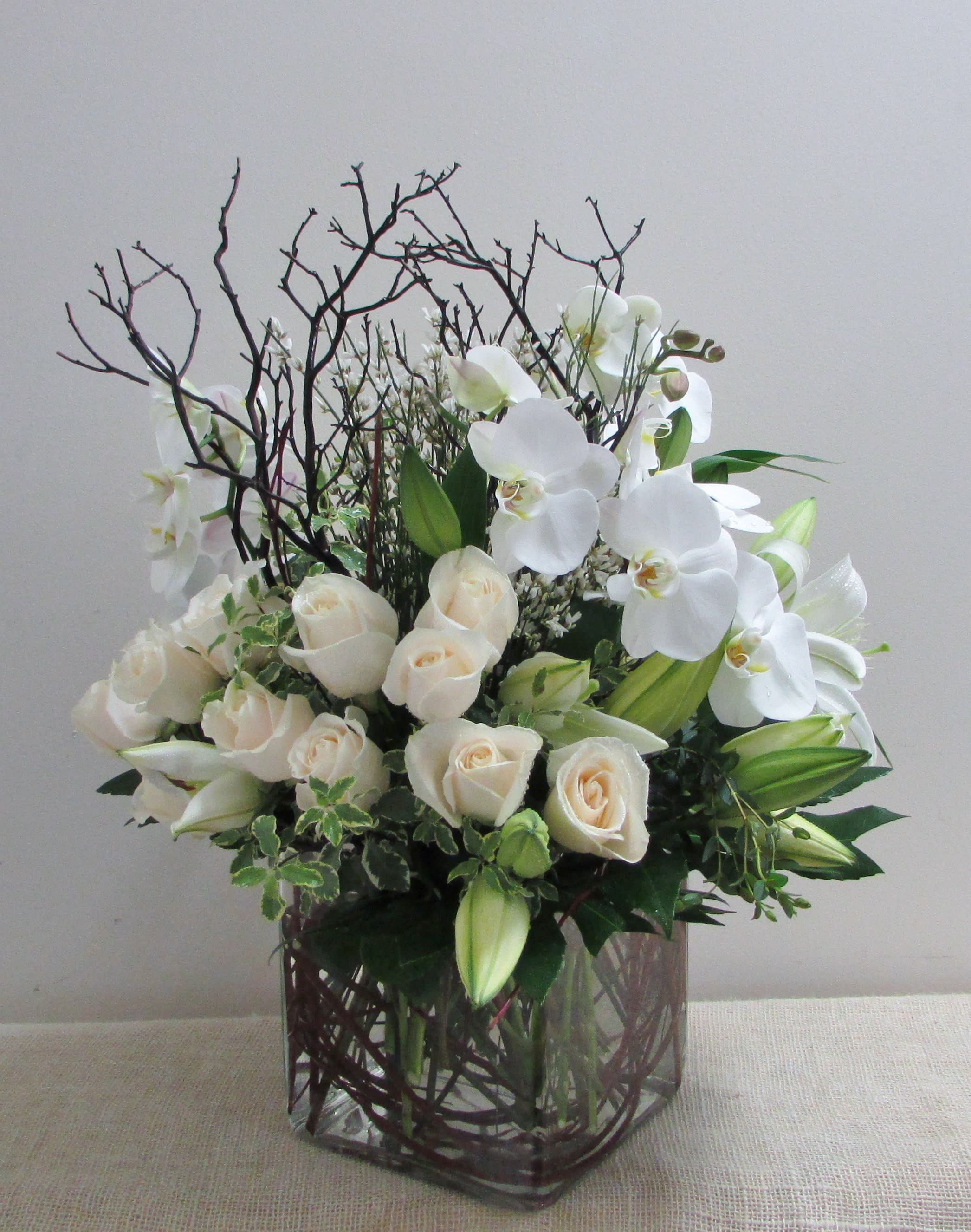 Enchanting - An large, enchanting all white arrangement. Carefully styled into a piece of art. This standout arrangement consists of roses, lilies, hydrangeas, other matching fillers and greens, wrapped in sticks for a unique and mesmerizing touch.  **Exact vase may not be available, may be substituted. Please give us a call for more details if the substitute is a concern. Ordering with advance notice will allow us to create the arrangement as similar as pictured. 