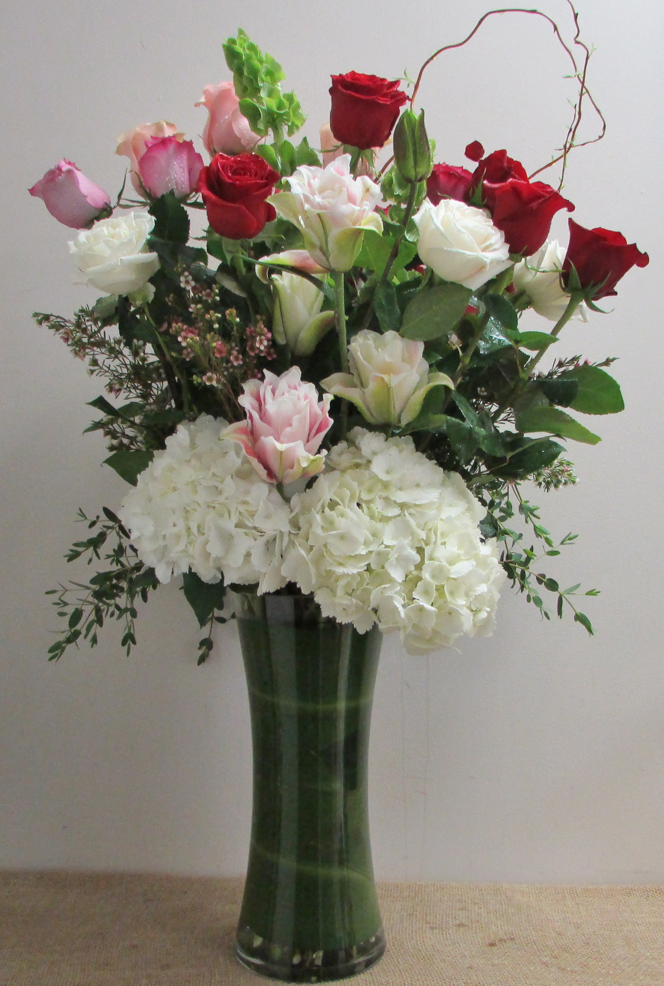 Tall bouquet of red, pink, and white roses with white hydrangeas in a glass vase