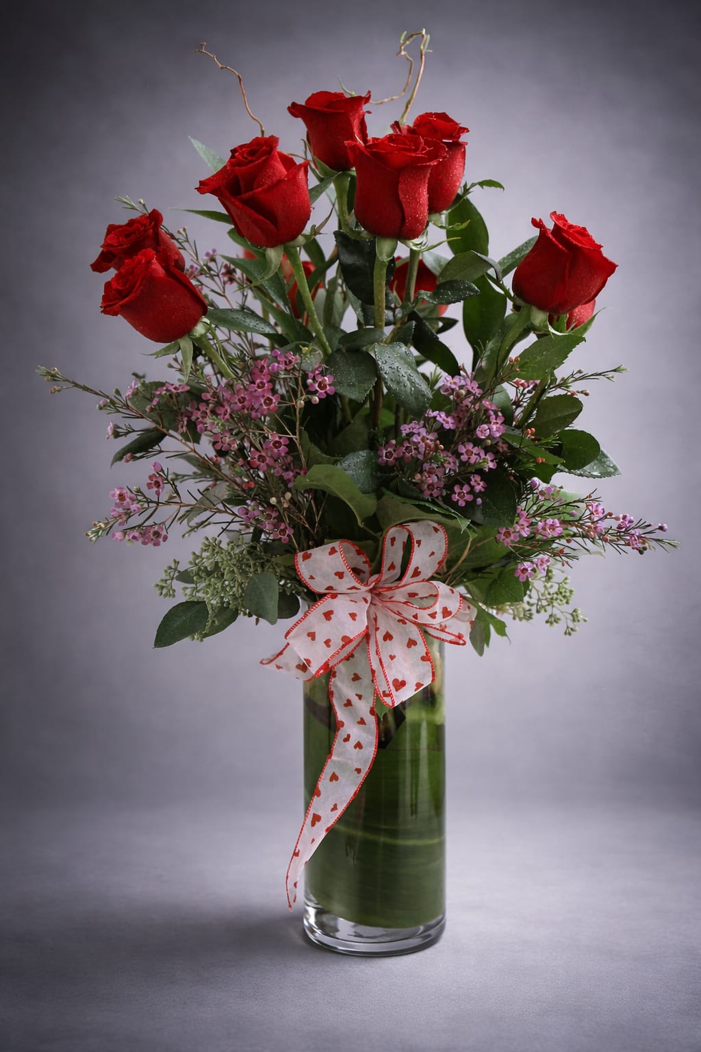 Red roses in a glass vase with a heart-patterned ribbon