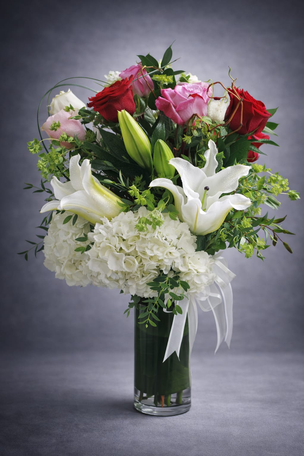 Bouquet of red and pink roses with white lilies in a glass vase