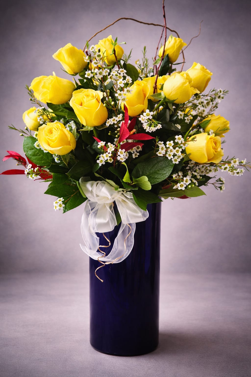 Yellow roses arranged in a tall blue vase with a white ribbon bow